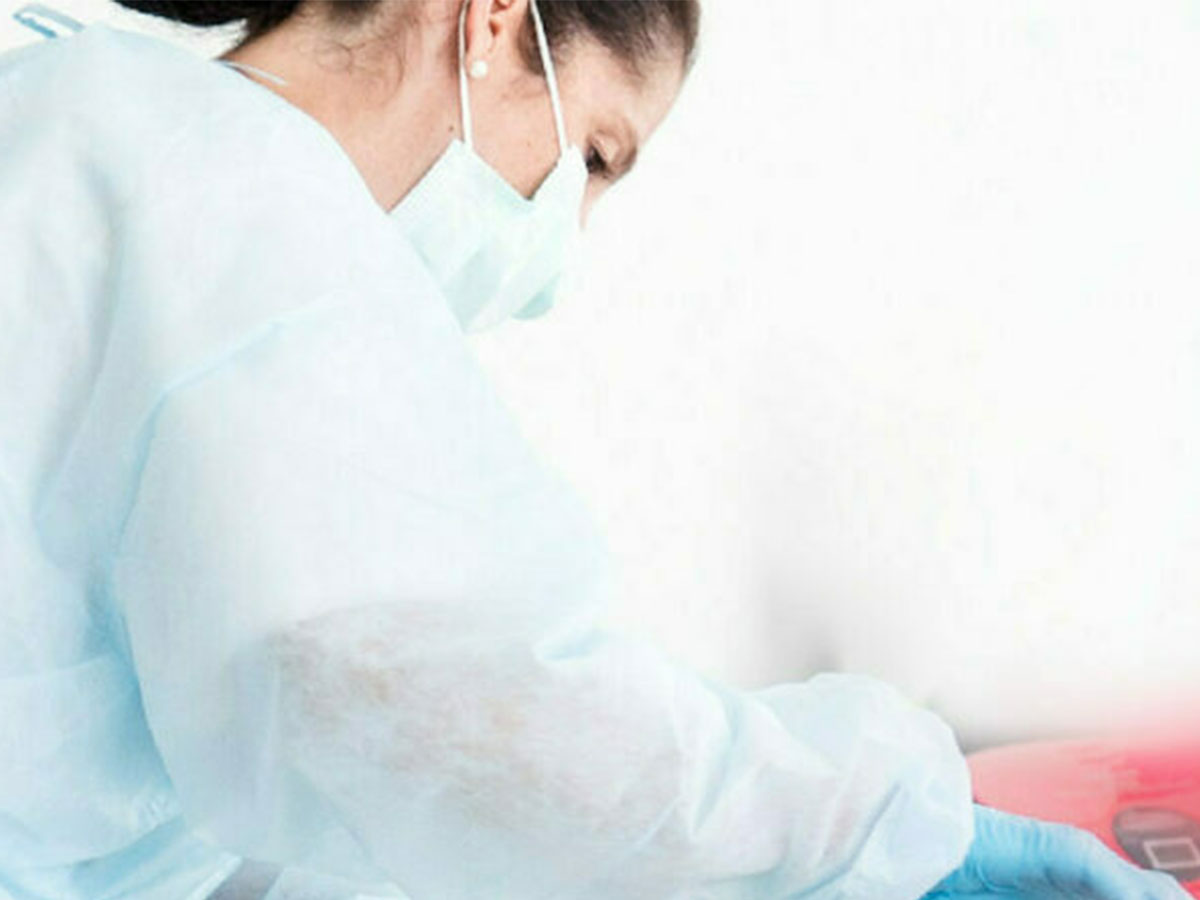 Researcher wearing protective clothing and a face mask examining something.