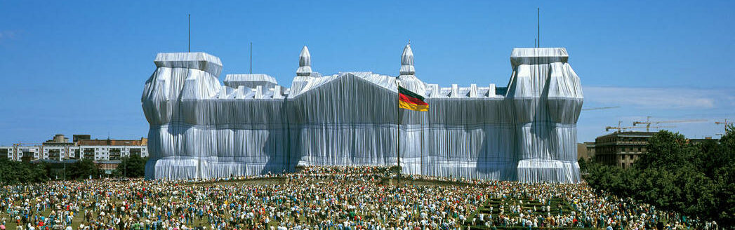 The Reichstag in Berlin covered in white foil, with many visitors in the foreground.