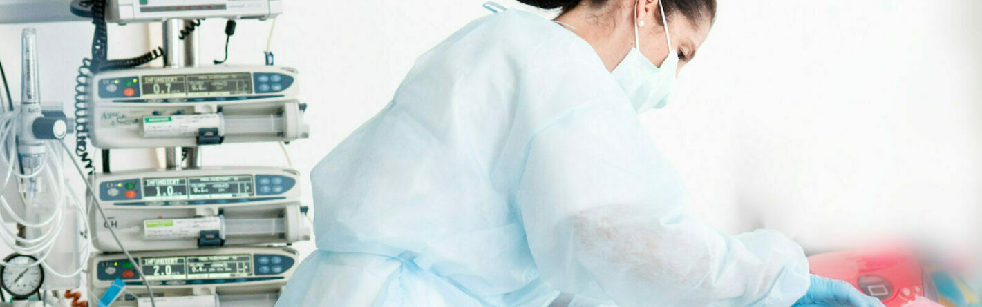 Researcher wearing protective clothing and a face mask examining something.