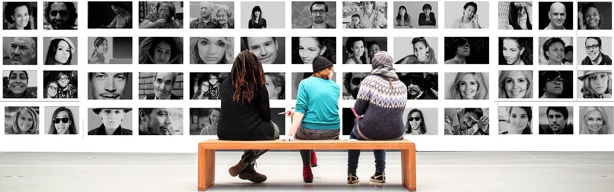 3 People sitting on a bench looking at many different pictures of people on the wall