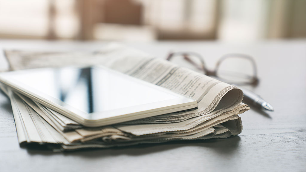 Newspaper and tablet, both lying on a table